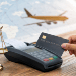 Cartão de crédito sendo passado em maquineta com boletos sobre a mesa, avião e rota dourada ao fundo em dupla exposição